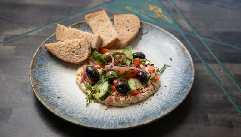 Ein Hauch von Orient — Hummus getoppt mit Tomate, Gurke, roter Zwiebel, Oliven, Kräutern und Sauerteigb bei Kaspio in Stade